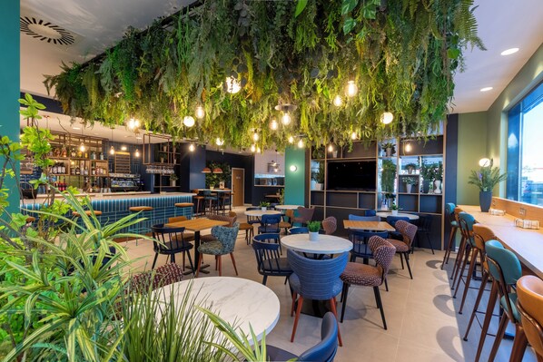A modern interior with hanging plants, round tables, and bar seating. - Travelodge Bilbao Sestao (Sestao)