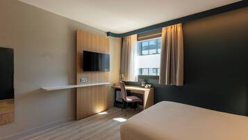 Una habitación de hotel con una cama, un escritorio con una silla, un televisor y una ventana con cortinas.