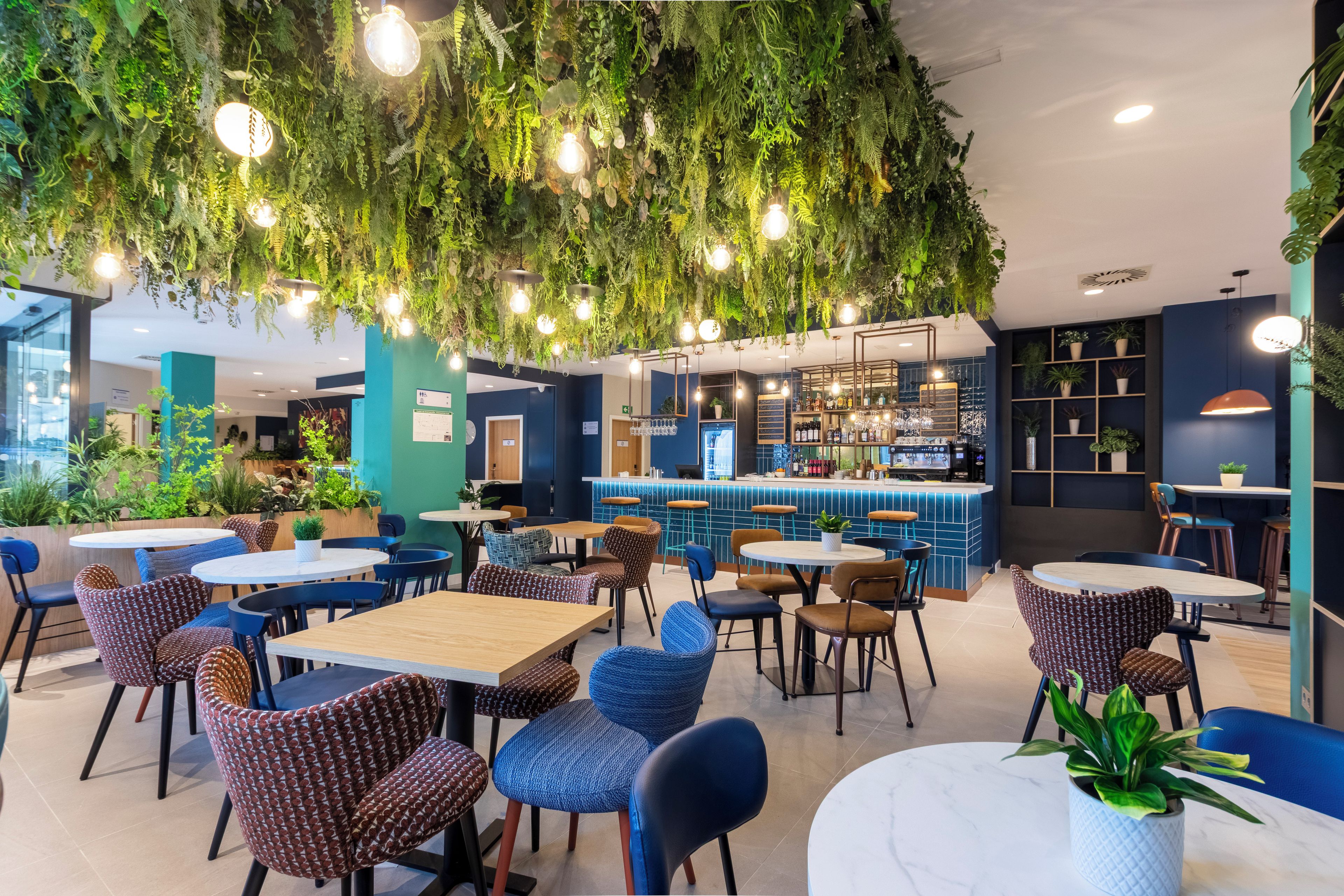 Un restaurante con plantas colgantes, mesas redondas y sillas.