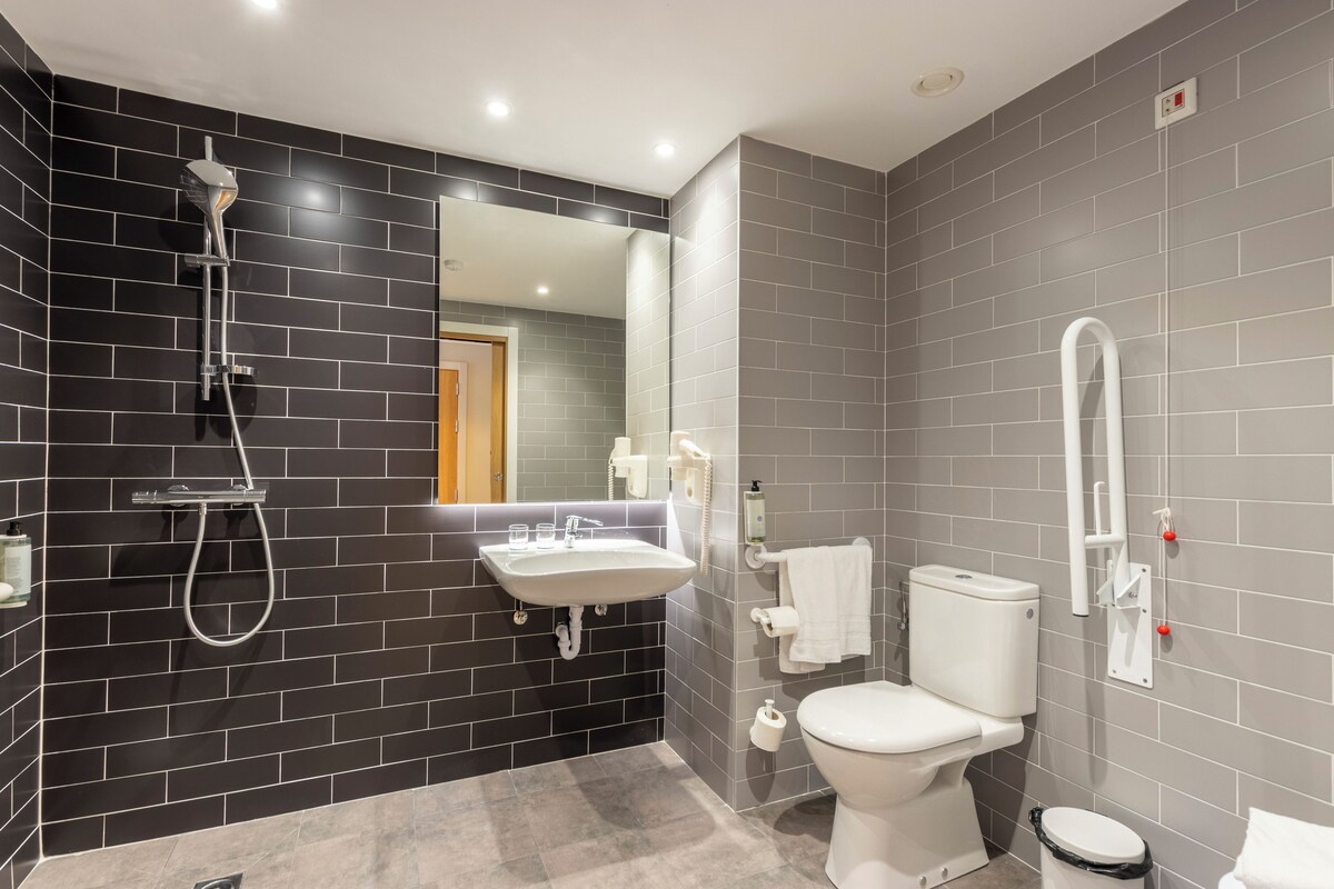 Une salle de bain moderne avec un mur recouvert de carreaux noirs et gris, un lavabo blanc, des toilettes et une douche.