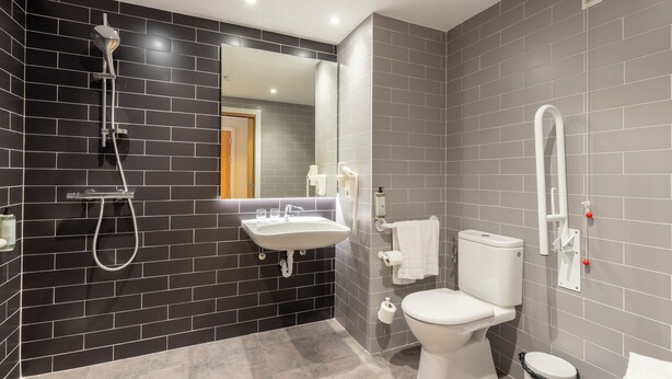 Een moderne badkamer met een betegelde muur in zwart en grijs, een wit wastafelmeubel, toilet en douche.