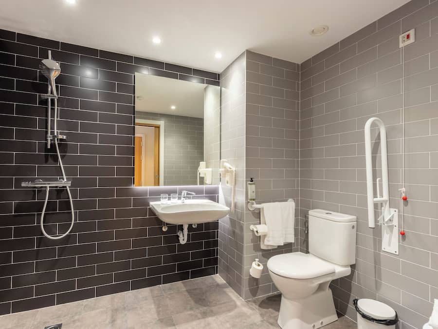 Et moderne badeværelse med væg i sort og grå fliser, en hvid vask, toilet og brusebad.