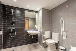 Une salle de bain moderne avec un mur recouvert de carreaux noirs et gris, un lavabo blanc, des toilettes et une douche.