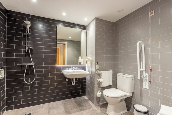 Une salle de bain moderne avec un mur recouvert de carreaux noirs et gris, un lavabo blanc, des toilettes et une douche.