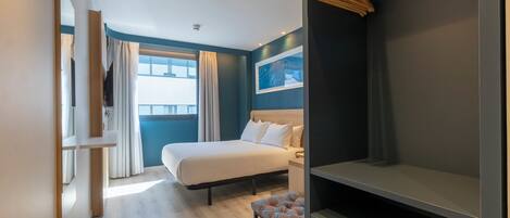 Una habitación de hotel moderna con cama, un banco, televisor y ventana con cortinas.