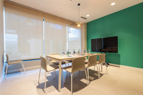 A conference room with a large table, chairs, a projector screen, and a TV on the wall. - Travelodge Bilbao Sestao (Sestao)