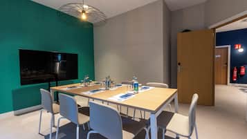 Una sala de conferencias con una mesa grande, sillas, un televisor de pantalla plana y una lámpara colgante.