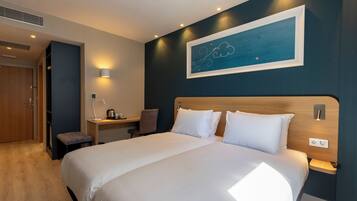 Ein Hotelzimmer mit einem großen Bett, einem Schreibtisch mit Stuhl, einem Wandbild und einer kleinen Bank.