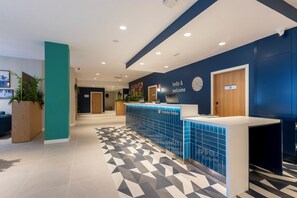 A reception area with a blue tiled counter, a clock, and a sign that reads 'hello & welcome'. - Travelodge Bilbao Sestao (Sestao)