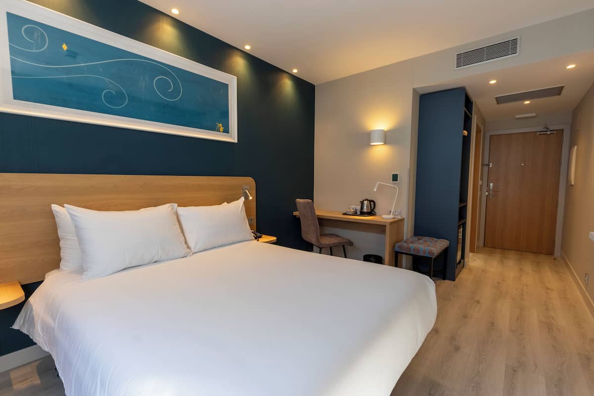 Hotelkamer met een groot bed, een bureau, een stoel, een tafeltje, een wandlamp en een deur.