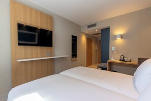 A hotel room with a bed, a TV mounted on a wooden panel, a bedside table with a lamp, and a small seating area. - Travelodge Bilbao Sestao (Sestao)