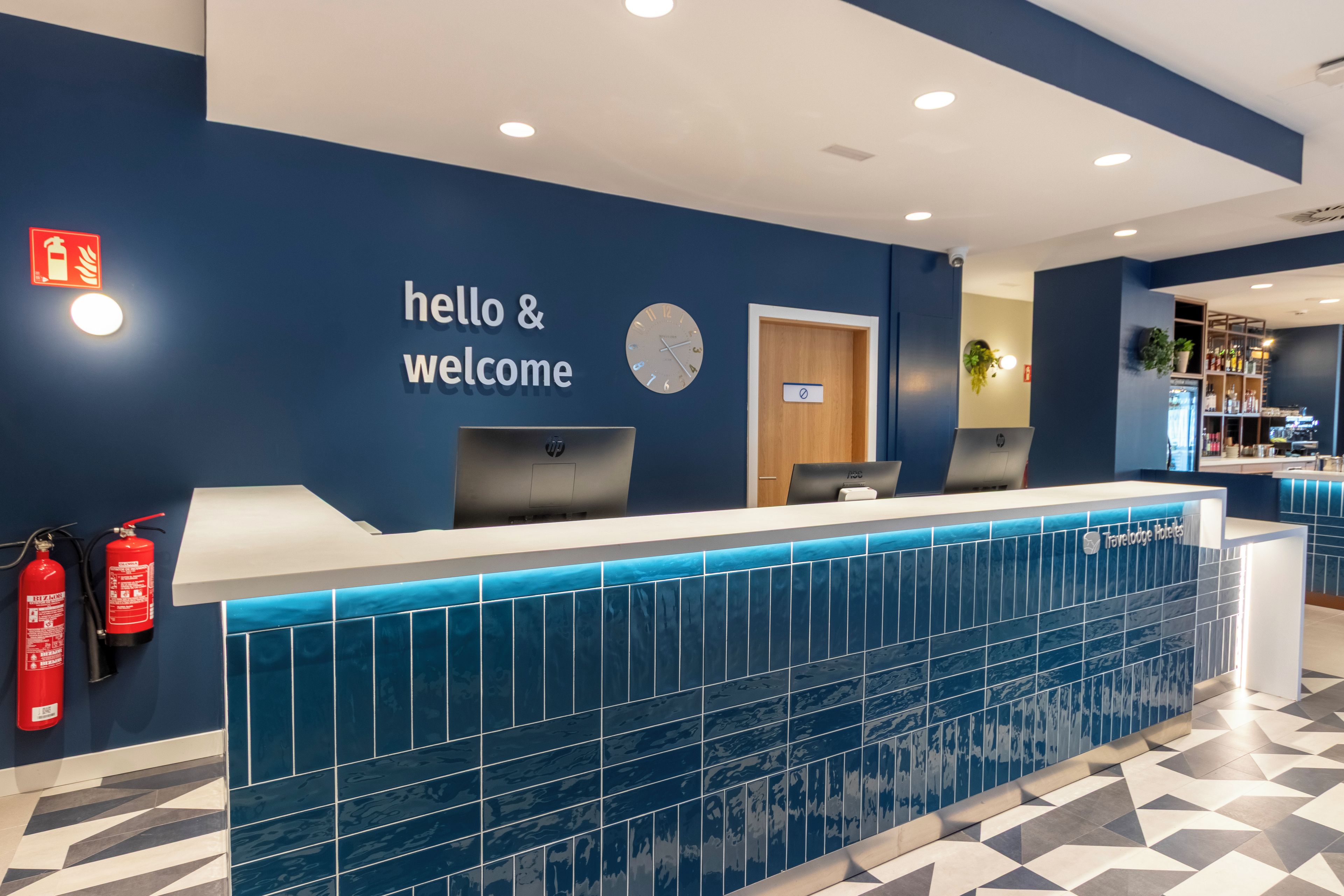 A reception desk with a 'hello & welcome' sign, a clock, and a fire extinguisher.