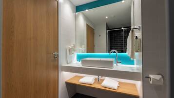 Un baño moderno con puerta de madera, paredes blancas, una pared azul de acento, un lavabo blanco, un mueble de tocador de madera y un espejo.