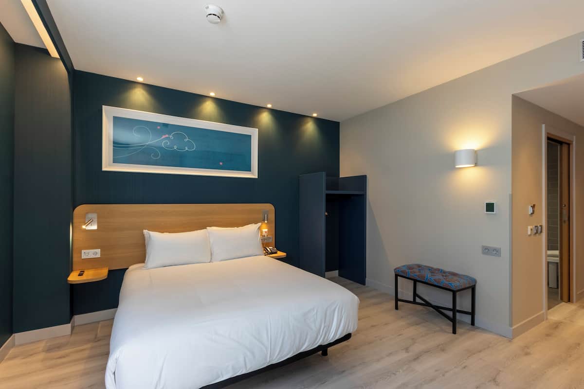 Een moderne hotelkamer met een groot bed, nachtkastjes, een bankje, een schilderij en een wandlamp.