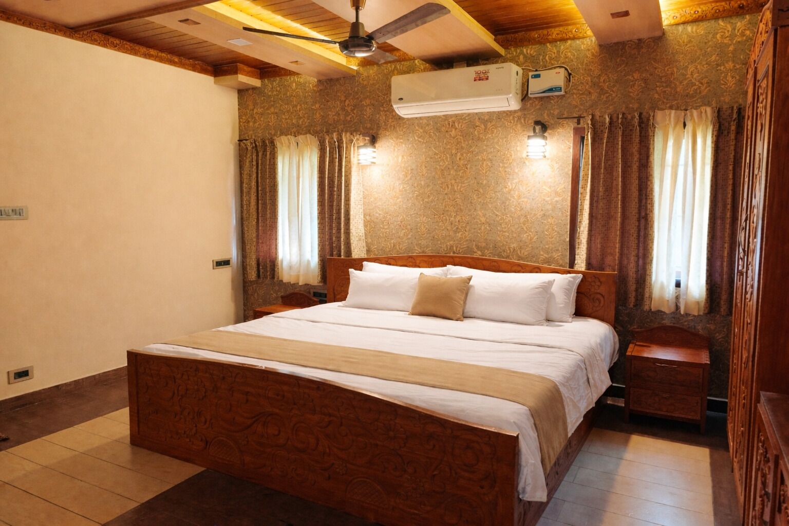 A bedroom with a wooden bed, a ceiling fan, an air conditioning unit, and patterned wallpaper.