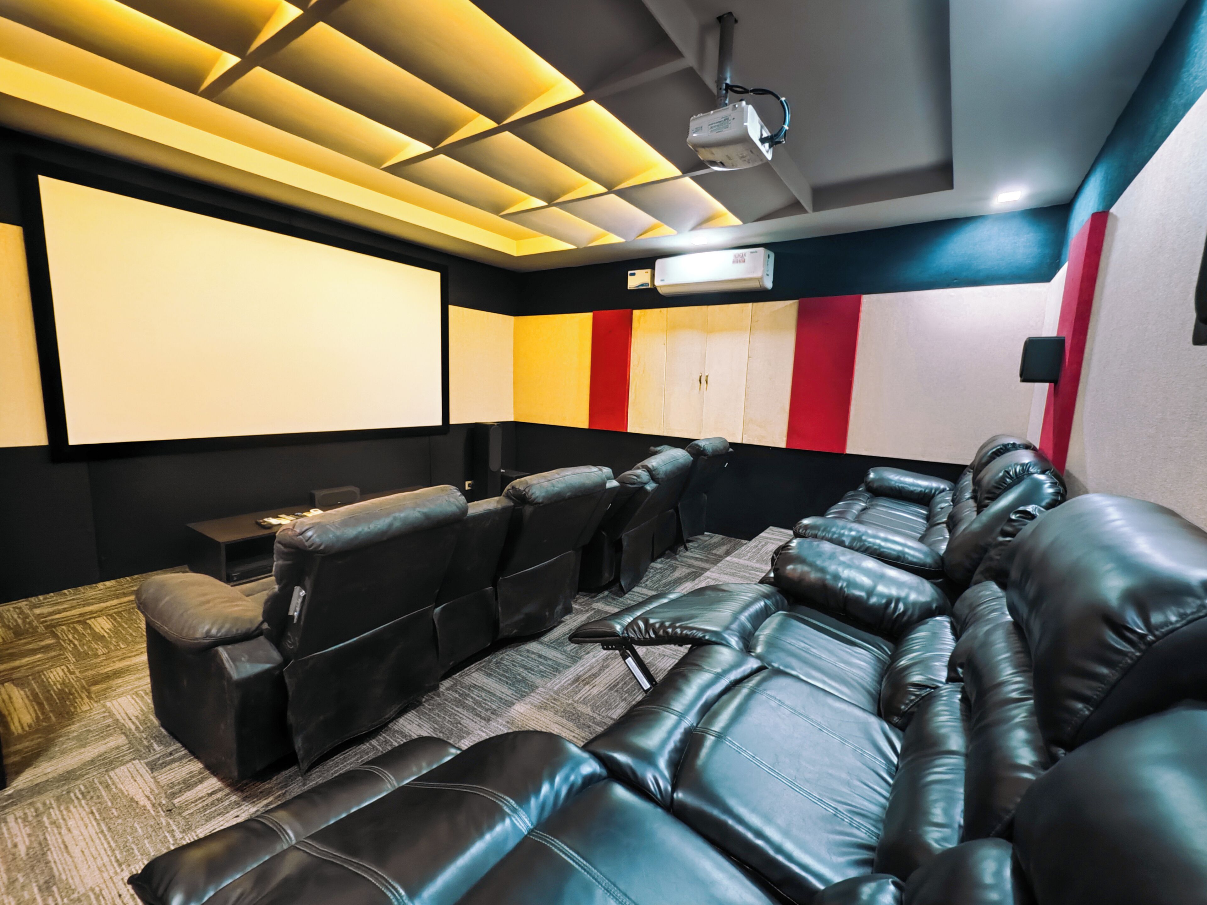Una sala de cine en casa con asientos de cuero reclinables, una pantalla grande y un proyector.