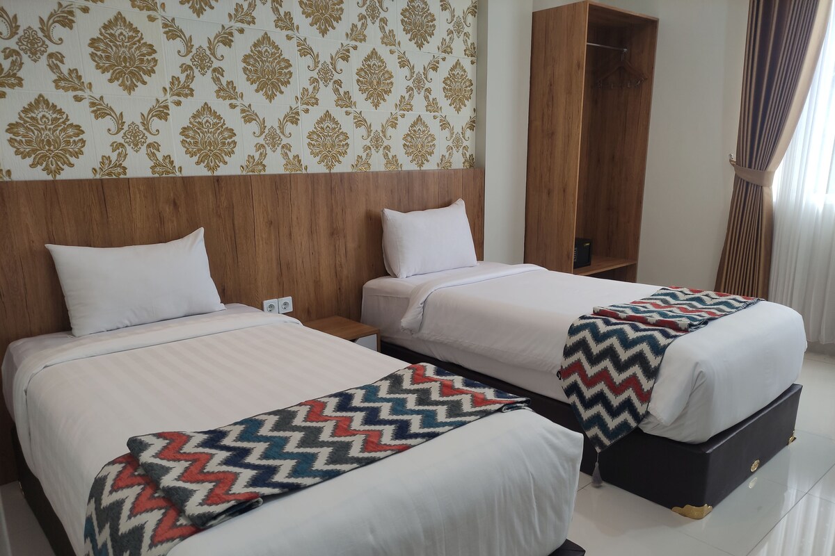 Habitación de hotel con dos camas, un cabecero de madera, un armario y un papel tapiz estampado.