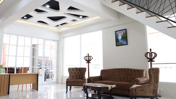 A spacious room with a high ceiling, a staircase, a large window, and a sofa. - Edu Hotel Y-skanam (Surabaya)