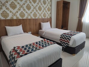 Habitación de hotel con dos camas, un cabecero de madera, un armario y un papel tapiz estampado.