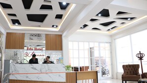 A hotel reception area with a marble counter, wooden paneling, and a large window. - Edu Hotel Y-skanam (Surabaya)
