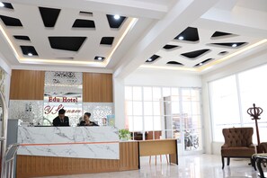 A hotel reception area with a marble counter, wooden paneling, and a large window. - Edu Hotel Y-skanam (Surabaya)