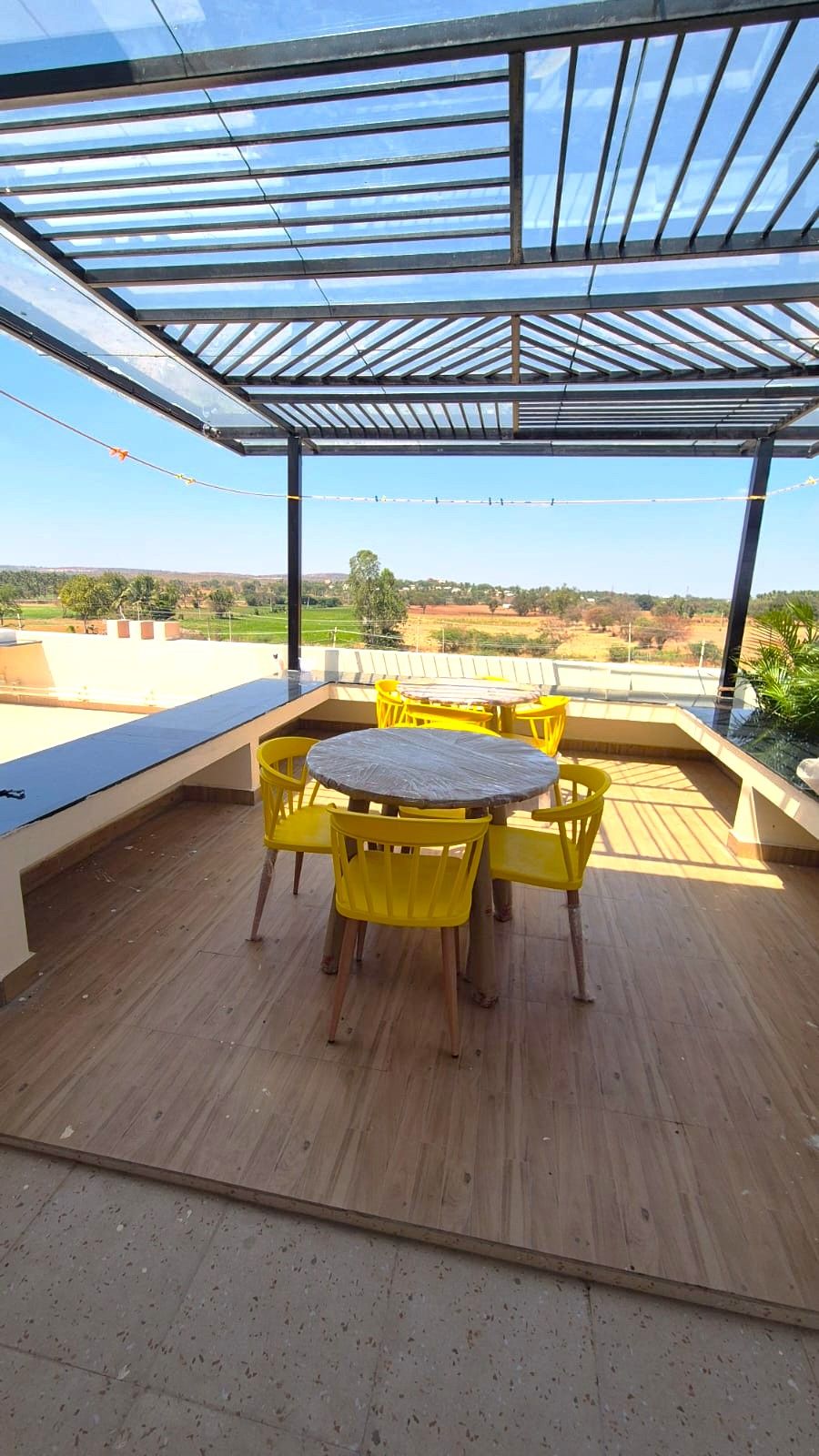 A covered outdoor area with a table and chairs, a view of the countryside, and a clear sky.