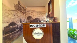 Un mostrador de recepción con un cartel que dice 'RECEPTION', una placa con una fecha y un mural que representa un paisaje.
