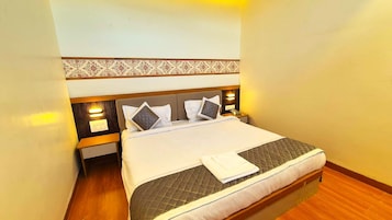 Quarto de hotel com cama, almofadas, mesa de cabeceira e criado-mudo.