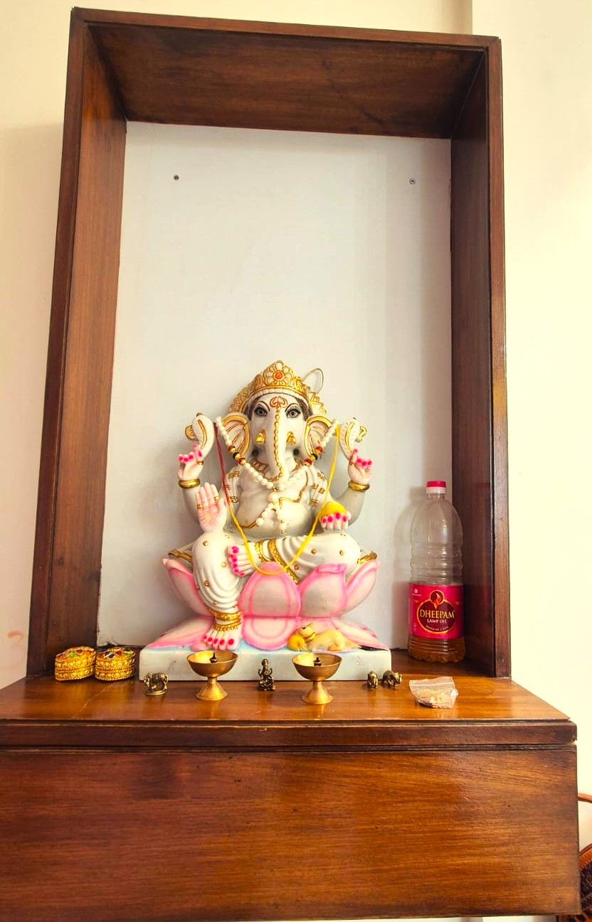 A framed statue of a deity on a wooden platform with a bottle of oil and small figurines.
