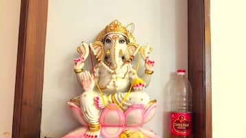 A framed statue of a deity on a wooden platform with a bottle of oil and small figurines.