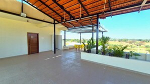 A covered outdoor area with a concrete floor, a wooden door, and yellow chairs. - Antilia Inn (Badami)