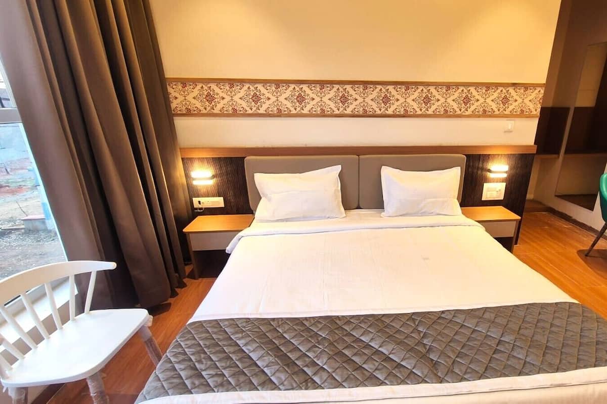 Una habitación de hotel con una cama, dos mesitas de noche con lámparas, una silla verde y una ventana con cortinas.