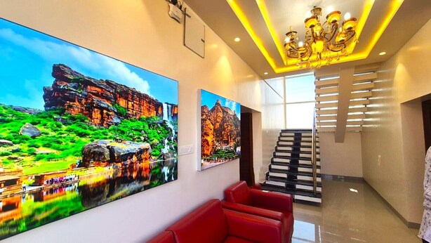 A modern hotel lobby with large landscape paintings, a staircase, and red seating. - Antilia Inn (Badami)