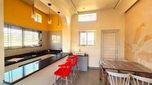Uma cozinha com bancada preta, banquetas vermelhas e uma mesa de jantar com cadeiras brancas.