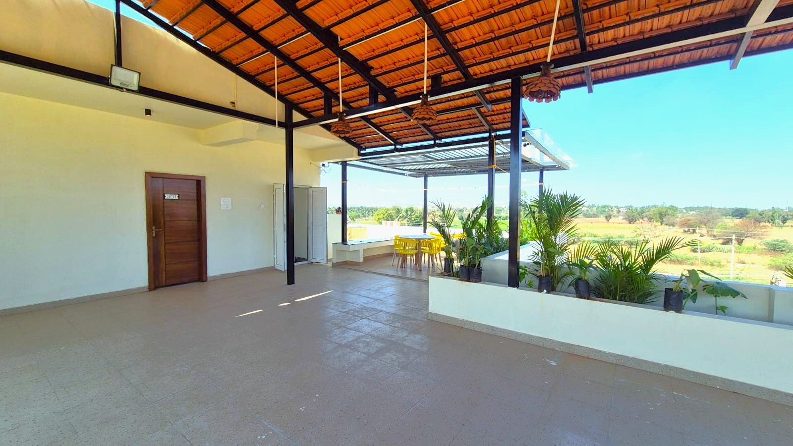 A covered outdoor area with a concrete floor, a wooden door, and yellow chairs.