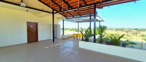 A covered outdoor area with a concrete floor, a wooden door, and yellow chairs.