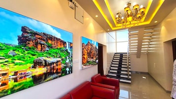 Um hall moderno de hotel com grandes pinturas de paisagens, uma escadaria e assentos vermelhos.