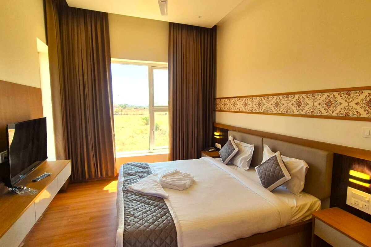 A hotel room with a bed, a TV, a wooden nightstand, and a window with curtains.