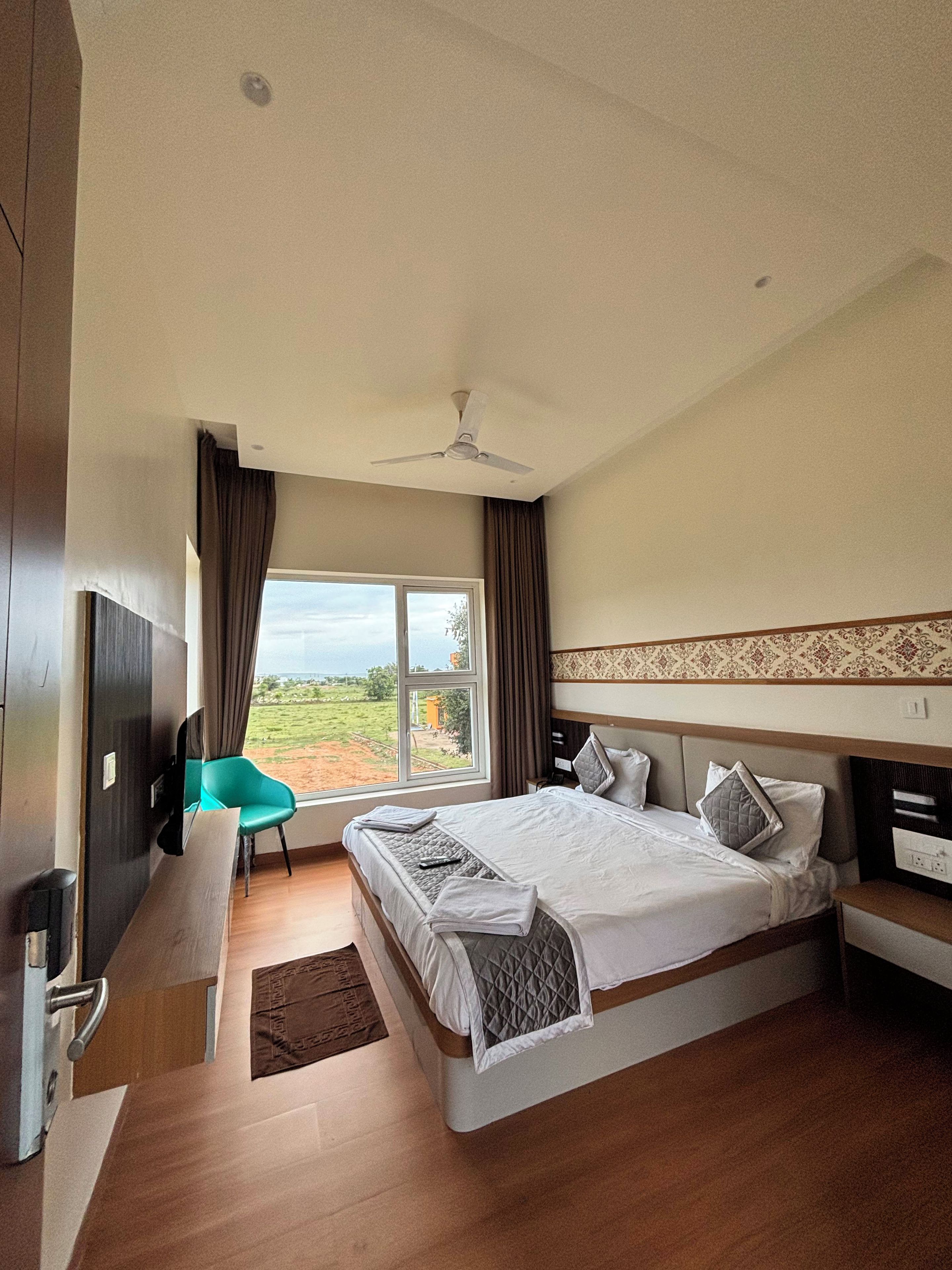 Ein Hotelzimmer mit einem Bett, einem Schreibtisch, einem Sessel, einem Fernseher und Blick ins Freie.