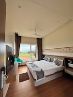 A hotel room with a bed, a desk, a chair, a television, and a view of the outdoors.