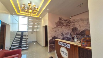 Un mostrador de recepción con un cartel que dice 'RECEPTION', una araña, una escalera y un mural de un templo.