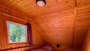 A small, wooden-paneled room with two beds, a window, and a ceiling light.