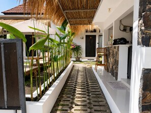 A narrow pathway with a patterned floor, surrounded by greenery and a thatched roof structure. - Susurro Villas (Kuta)