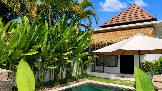 A poolside area with a thatched-roof structure, a lounge chair, and lush tropical plants. - Susurro Villas (Kuta)