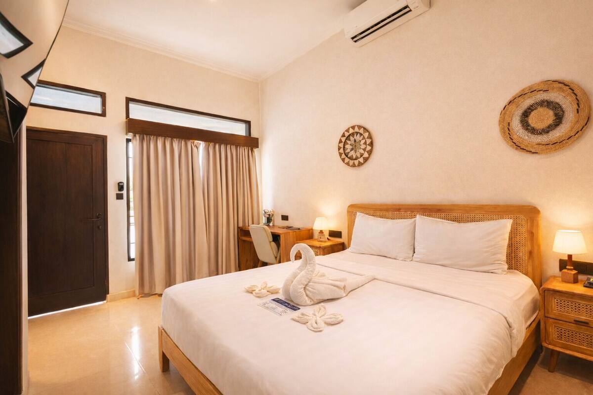 A hotel room with a bed, a desk, a chair, a door, and a window with curtains.