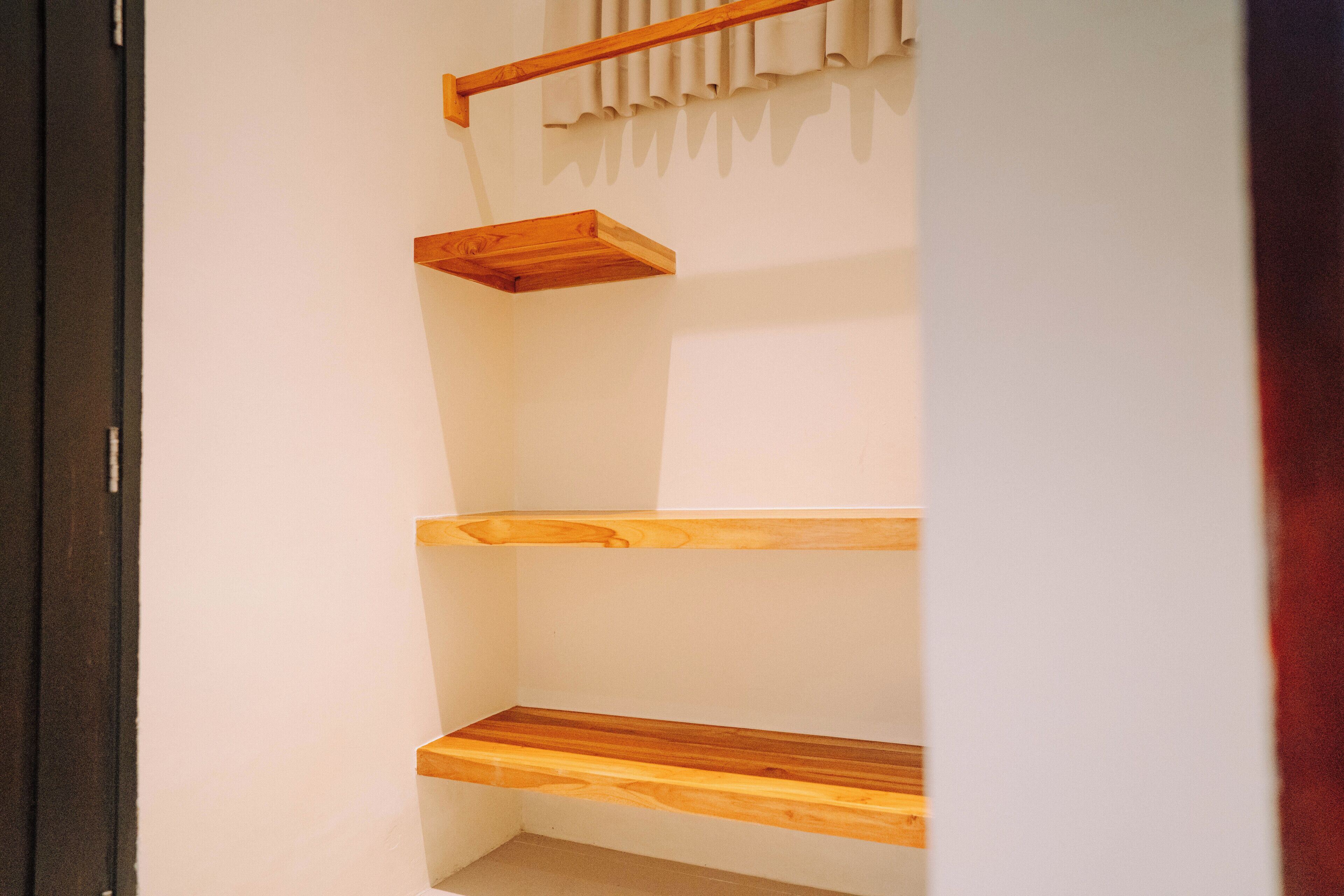 A corner of a room with a wooden shelf unit against the wall.