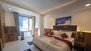 A modern hotel room with a large bed, wooden headboard, and a view of a mountain. - Hotel Vishnu Sarovar (Badrinath)