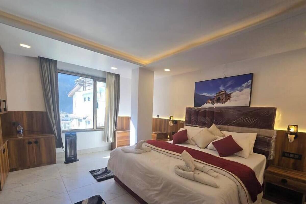 Una habitación de hotel moderna con una cama grande, cabecera de madera y vistas a la montaña.
