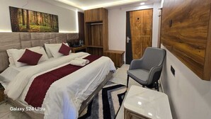 A modern hotel room with a Galaxy S24 Ultra bed, a grey armchair, a wooden wardrobe, and a large forest-themed painting on the wall. - Hotel Vishnu Sarovar (Badrinath)