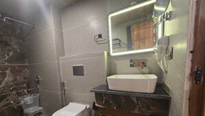 A bathroom with a toilet, a sink, a shower, and a mirror. - Hotel Vishnu Sarovar (Badrinath)